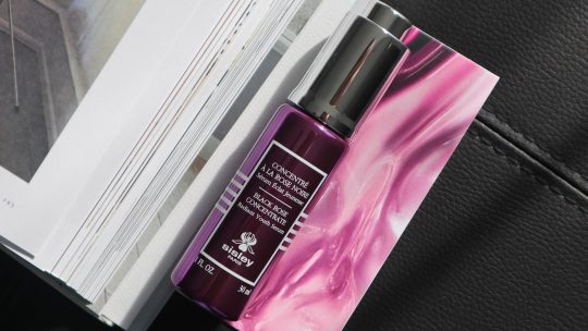 Sisley Paris Black Rose Concentrate bottle sitting elegantly on a marble vanity next to fresh pink roses